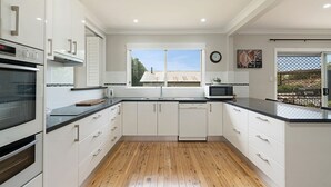 A modern kitchen with white cabinets, a wooden floor, a microwave, and a large window.