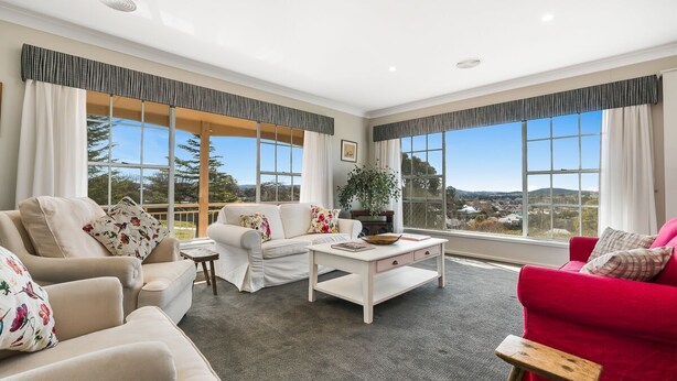 A spacious living room with a beige sofa, a red sofa, and a white coffee table. Large windows offer a view of the outdoors.