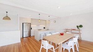 A modern kitchen with white cabinetry, a stainless steel refrigerator, and pendant lighting.