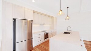 A modern kitchen with stainless steel appliances, white cabinetry, and wooden flooring.