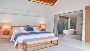 A modern bedroom with a large bed, bedside lamps, a bench, and a view of a bathroom with a bathtub.