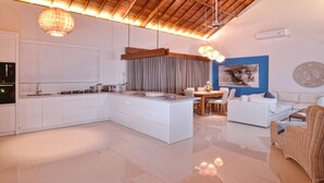A modern kitchen with a central island, a dining area with a table and chairs, and a living area with a sofa and a wicker chair.