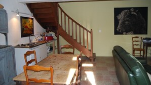 Ein Essbereich mit einem Holztisch und Stühlen, eine Küche im Hintergrund, eine Treppe und ein grünes Sofa.