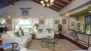 Ein geräumiges Wohnzimmer mit weißen Sofas, einem Glastisch und Blick aufs Meer.