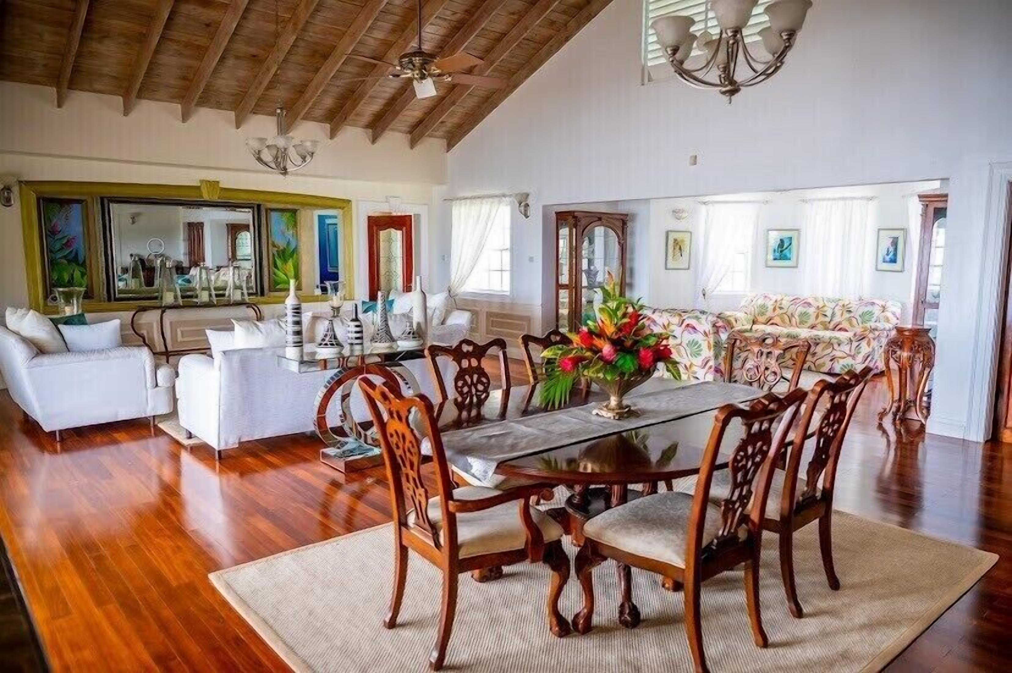 Un salón espacioso con techo de madera, una zona de comedor con mesa de vidrio y un sofá de estampado floral colorido.