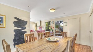 Un coin repas avec une table et des chaises en bois, un tableau abstrait noir accroché au mur, et une cuisine en arrière-plan.