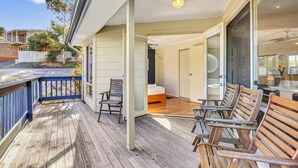 Une terrasse en bois avec des chaises et un lit, visibles à travers une porte ouverte.