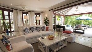 A spacious living room with a white sofa set, a glass coffee table, and a view of the outdoor patio area. - Stunning, private villa on Barbados' Platinum west coast. (Gibbs)