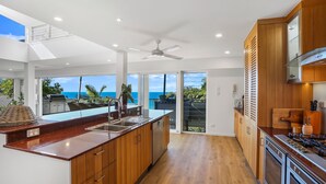 Una cocina moderna con una isla grande, armarios de madera y vista al océano.