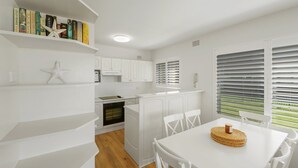 Une cuisine moderne avec des meubles blancs, un four encastré et un coin repas comprenant une table et des chaises blanches.