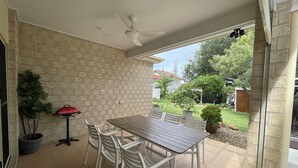 An outdoor patio with a table and chairs, a ceiling fan, and a view of a garden and neighboring houses. - "Oxley House" - Scarborough Q 4020 (Scarborough)
