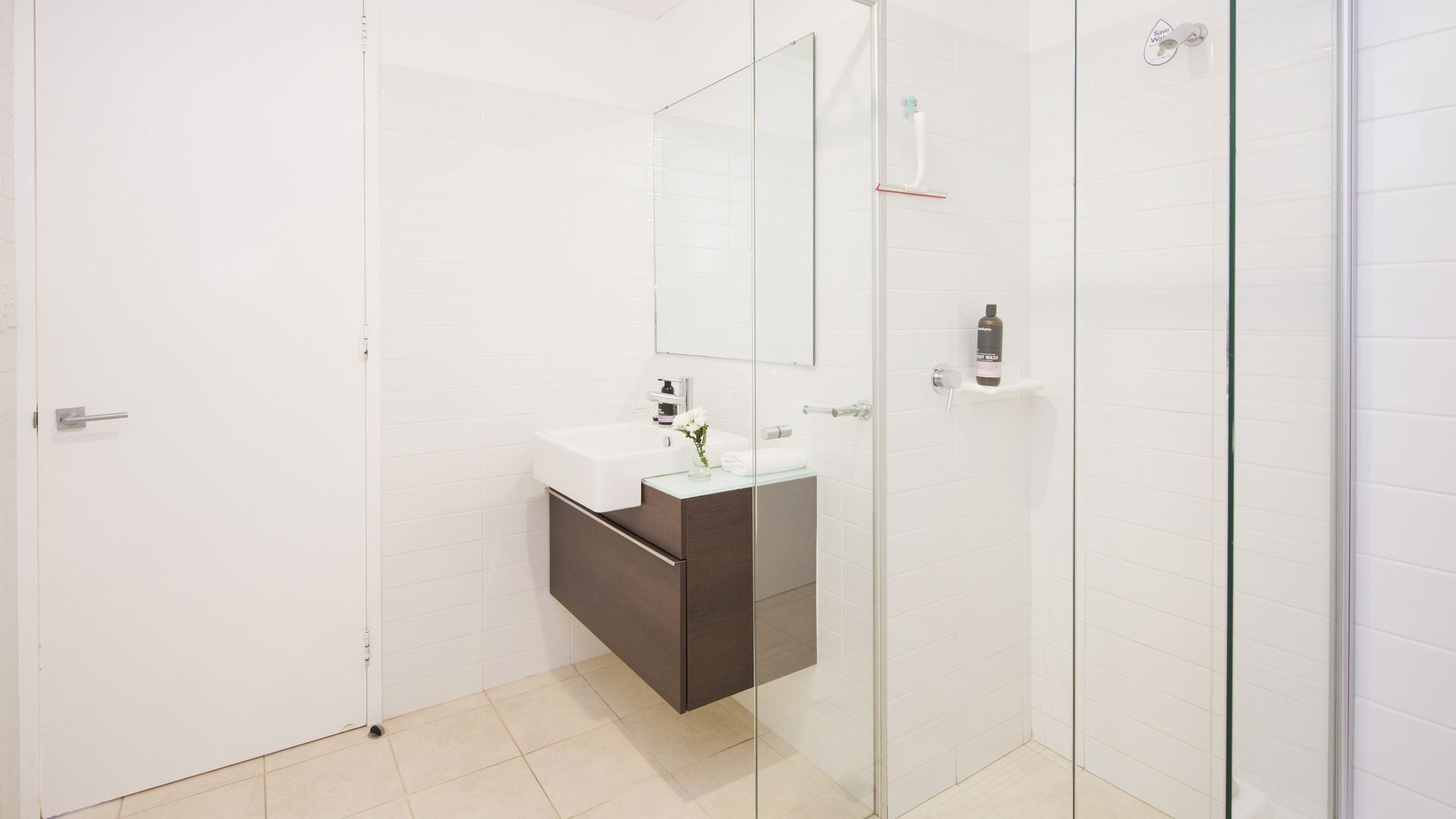 Un bany modern amb plat de dutxa de vidre, un lavabo blanc i un moble sota d'aquest de fusta fosca, i un mirall sobre el lavabo.