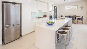Una cocina moderna con un refrigerador de acero inoxidable, gabinetes blancos, una isla central con taburetes y un comedor con mesa y sillas.