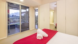 Habitación de hotel con una cama, una colcha roja y un ventanal corredero que da a una zona de estar al aire libre.
