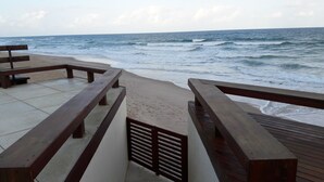 Une terrasse en bois avec des bancs, donnant sur une plage et l’océan.