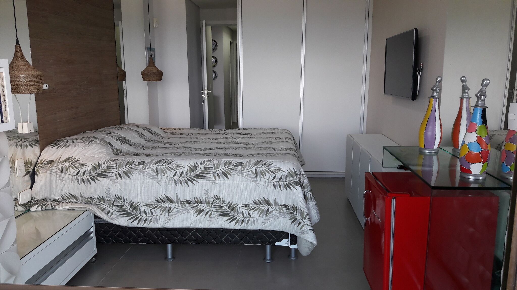 A bedroom with a bed, bedside table, dresser, and a TV mounted on the wall.