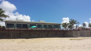 Un immeuble situé en bord de mer, doté d’un balcon, d’une antenne parabolique et de palmiers en arrière-plan.