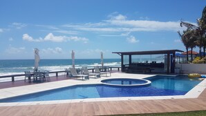 Un espace piscine avec des chaises longues et des parasols, offrant une vue sur l’océan.