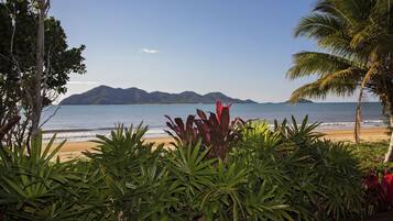 A tropical beach with a view of mountains in the distance, surrounded by lush greenery.