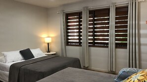 Une chambre d’hôtel avec un lit, une table de chevet avec une lampe et une fenêtre avec des stores.