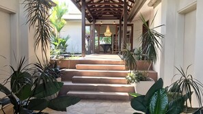 Un escalier extérieur abrité, menant à l’entrée d’un bâtiment, et entouré de plantes en pot.
