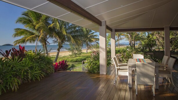 Une terrasse en bois, agréée de mobilier d’extérieur, qui offre une vue sur une plage et l’océan.