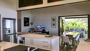 A modern kitchen with a built-in refrigerator, a dining area with a table and chairs, and a view of a lush garden through an open door.