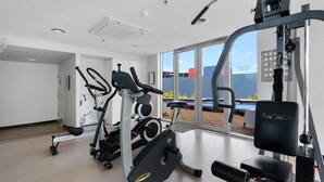 A modern gym with various exercise equipment, large windows offering a view of a pool and building outside. - The Penthouse with Views (Victor Harbor)