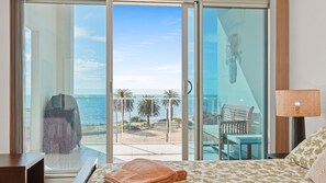 A hotel room with a large sliding glass door leading to a balcony with a view of the ocean and palm trees.