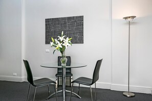 A modern dining area with a glass table, two black chairs, a vase with white flowers, and a floor lamp. - Sydney- CLD01 Bridge Street - Modern 1BR with Rooftop Pool in the Heart of Sydney CBD (Sydney)