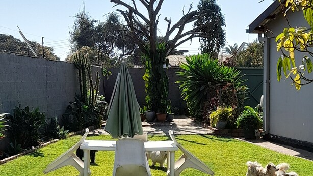 Une terrasse avec une table et des chaises, entourée d’une pelouse bien entretenue et de diverses plantes.