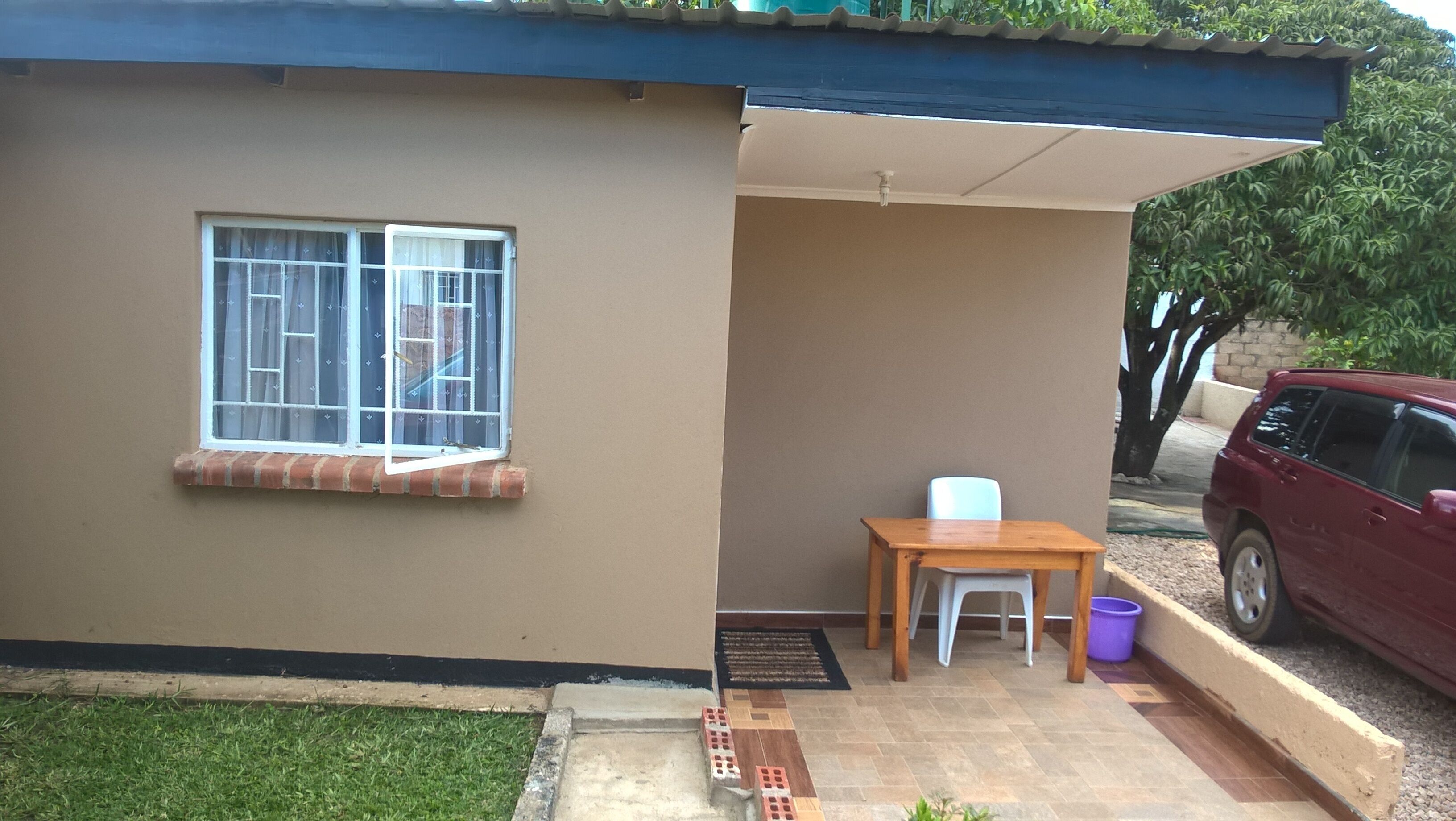 Uma casa térrea com uma janela, uma mesa pequena e uma cadeira na parte externa.