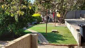 Un chemin pavé mène à une zone herbeuse où se trouve un petit arbre et un banc en béton.