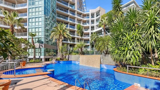 A swimming pool surrounded by palm trees and a modern building with balconies.