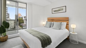 A modern hotel room with a large bed, a view of the city, and a framed artwork on the wall.