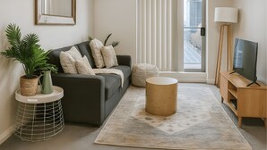 A modern living room with a grey sofa, a round coffee table, a floor lamp, and a TV stand.