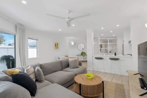 A modern living room with a sofa, a round wooden table, and a kitchen area with a bar.