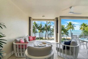Un balcon offrant une vue sur les palmiers et l’océan, aménagé avec un canapé, des fauteuils et une table.