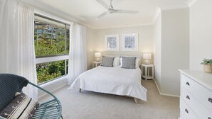 Ein Schlafzimmer mit einem Bett, zwei Nachttischen, einem Sessel, einer Kommode und einem Deckenventilator.