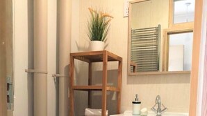 Une salle de bain comprenant des toilettes, un lavabo, un miroir et une étagère en bois où sont posées des serviettes.