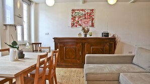 Un coin repas avec une table et des chaises en bois, un canapé beige et un meuble en bois contenant une horloge et une radio.