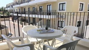 Un balcon avec une table ronde et deux chaises, donnant sur un immeuble doté de nombreux balcons et fenêtres.