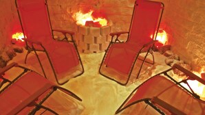 Deux fauteuils rouges sont placés face à un mur de pierre, près d’un foyer.