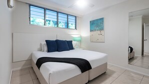 A bedroom with a bed, a window, a painting, and a mirror. - Lagoon Lodge 105, Beachfront Apartment on Hamilton Island (Hamilton Island)