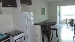 Een keuken met een koelkast met dubbele deuren, een fornuis en een eethoek met een tafel en stoelen.