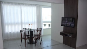 Een eethoek met een ronde tafel en stoelen, een televisie aan de muur en een balkon met uitzicht.