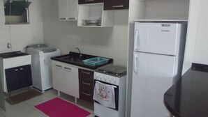 Een kleine keuken met witte kastjes, een spoelbak, een kookplaat en een koelkast.