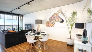 Una zona de menjador moderna amb una taula de vidre, cadires blanques i un quadre de zebra a la paret.