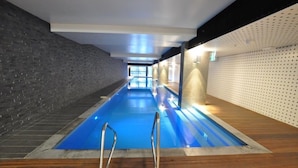 Una piscina interior amb sòl de fusta, aigua blava i una paret de maó a un costat.