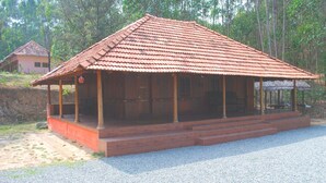 A wooden structure with a tiled roof, a porch, and a gravel ground. - Nature Castle-A traditional kerala style  (Vattavada)